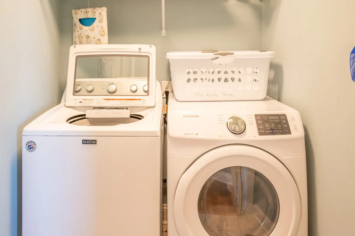 A clean and organized laundry area with a washing machine, dryer, and laundry basket. The space is practical and signals convenience, supporting options for bringing your own linens or using the linen service.