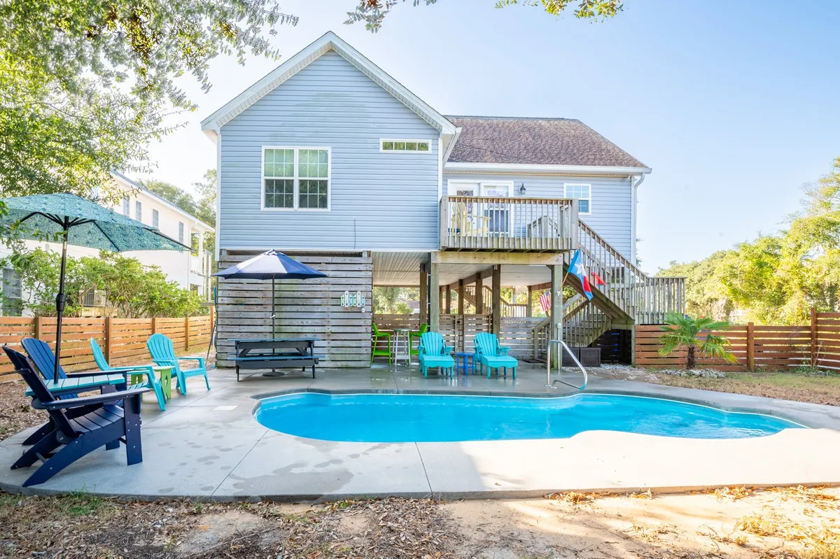 This exterior image features a sparkling swimming pool surrounded by a spacious deck area, with lounge chairs, a large umbrella for shade, and a view of the house exterior in the background. The setting is perfect for both sunbathing and social gatherings, offering a glimpse of the inviting pool and adjacent relaxation spaces.