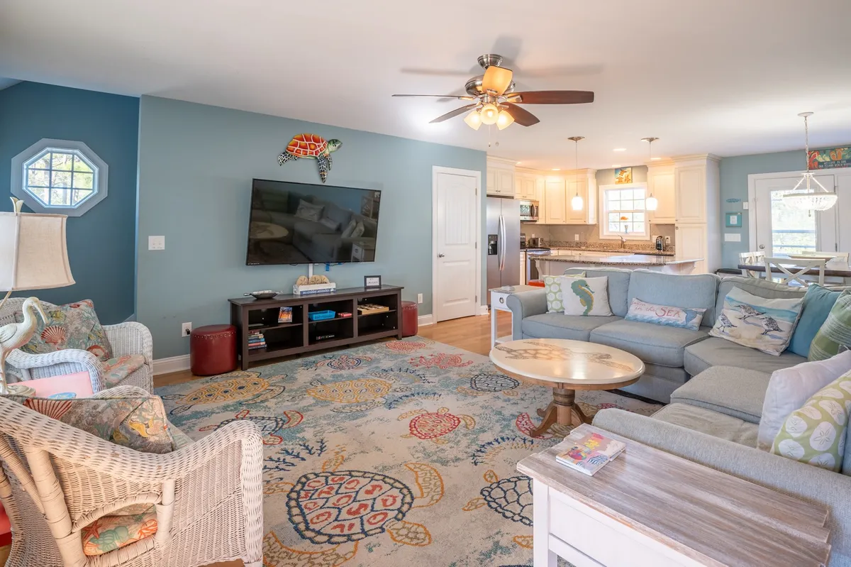 A bright, open living room featuring an oversized sectional sofa, a colorful area rug, and a flat-screen TV. Comfortable lighting and plenty of seating invite everyone to settle in for movie nights or casual conversation.