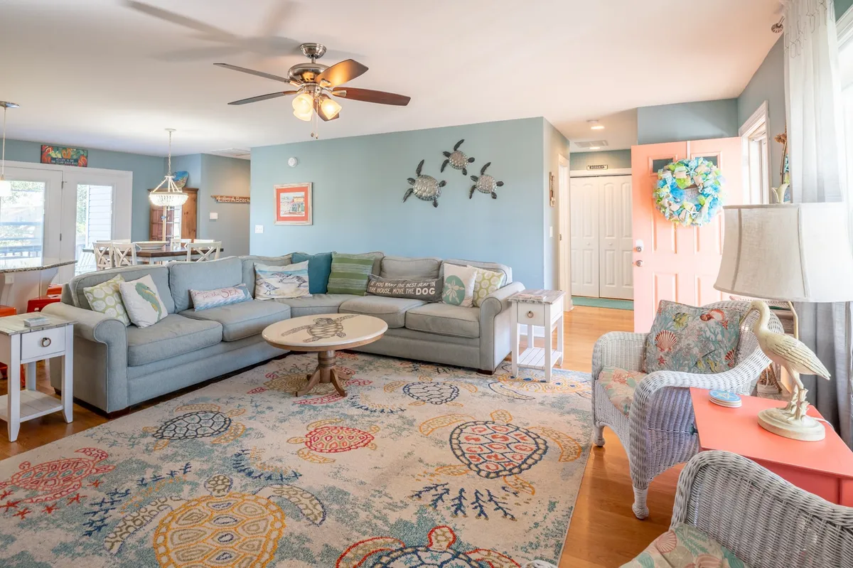 The image captures a bright, open living area with a comfortable sectional sofa, a colorful area rug, decorative wall art, and a vividly painted entrance door. The space feels cheerful and immediately welcoming, ideal for gatherings or relaxing after exploring the area.