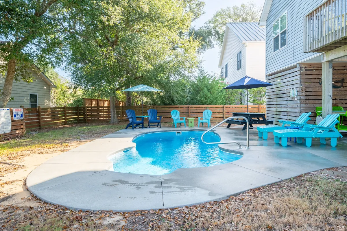 An inviting private swimming pool surrounded by colorful lounge chairs and a patio umbrella, set in a sun-soaked outdoor area perfect for relaxation and play after beach or park fun.