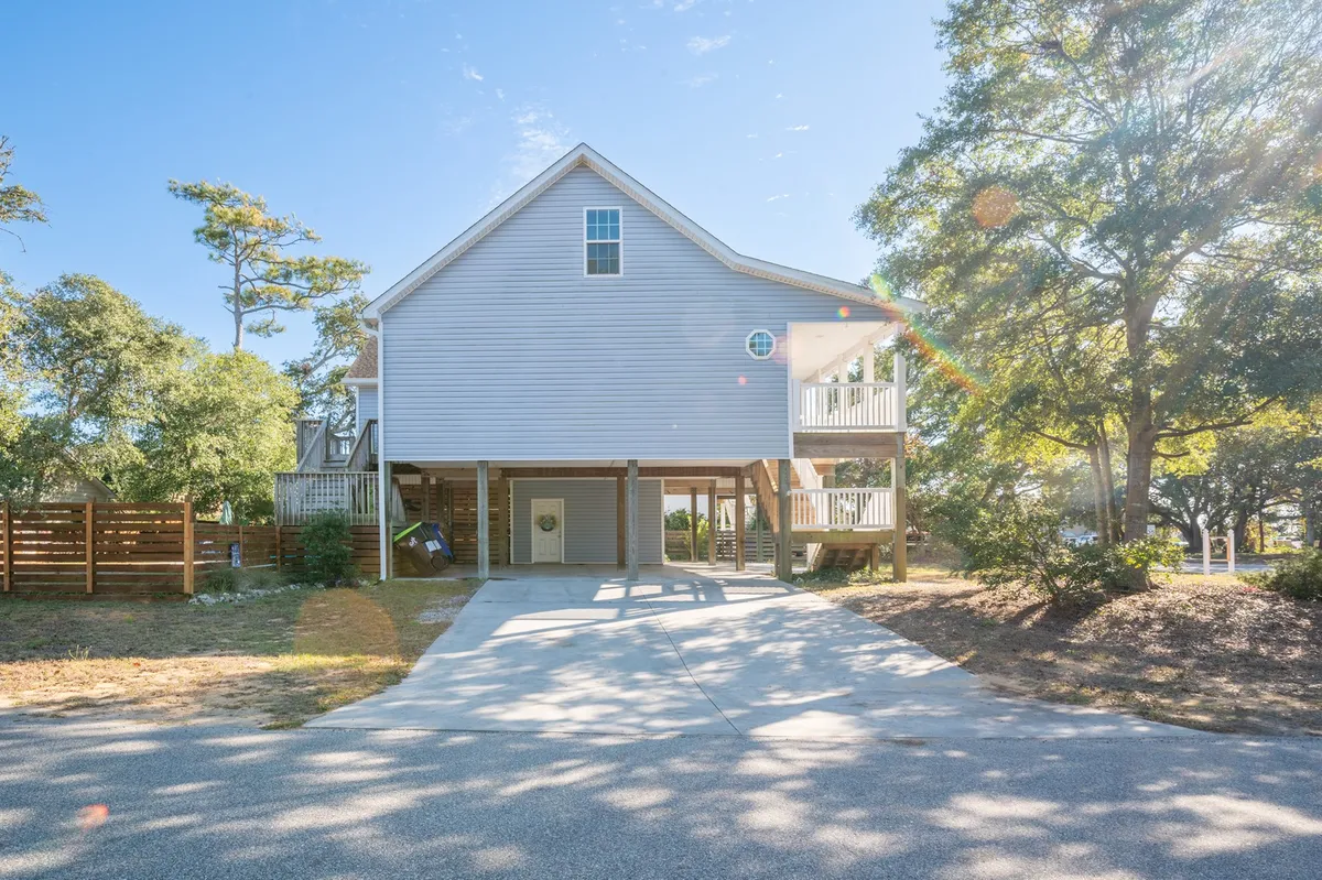 This image features the exterior structure of the Gypsy Rose Beach House, showcasing its welcoming façade, driveway, and surrounding trees. The inviting porch and tranquil outdoor setting highlight both the house's ample space and its suitability for group arrivals and outdoor gatherings.