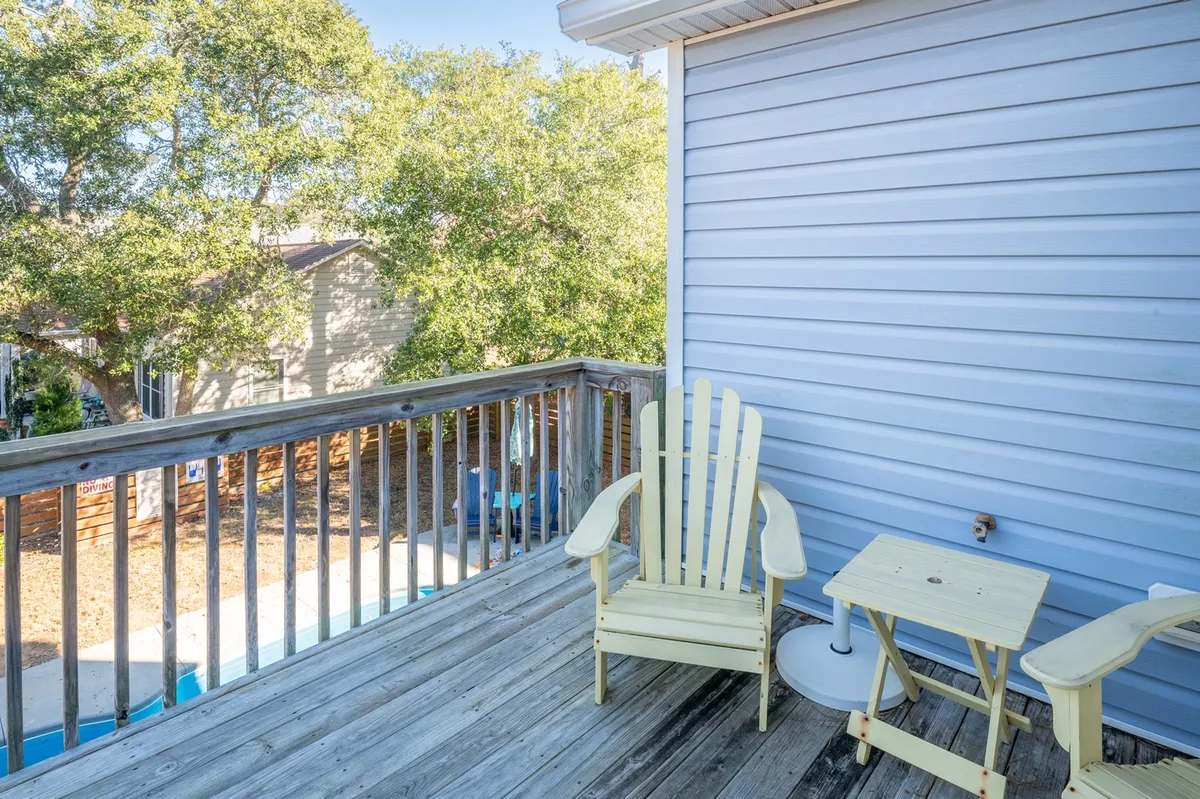 A tranquil porch scene with yellow Adirondack chairs, a small side table, and a wooden railing framed by leafy trees. The porch offers a cozy vignette perfect for morning coffee, reading, or board games in a shaded, peaceful setting.