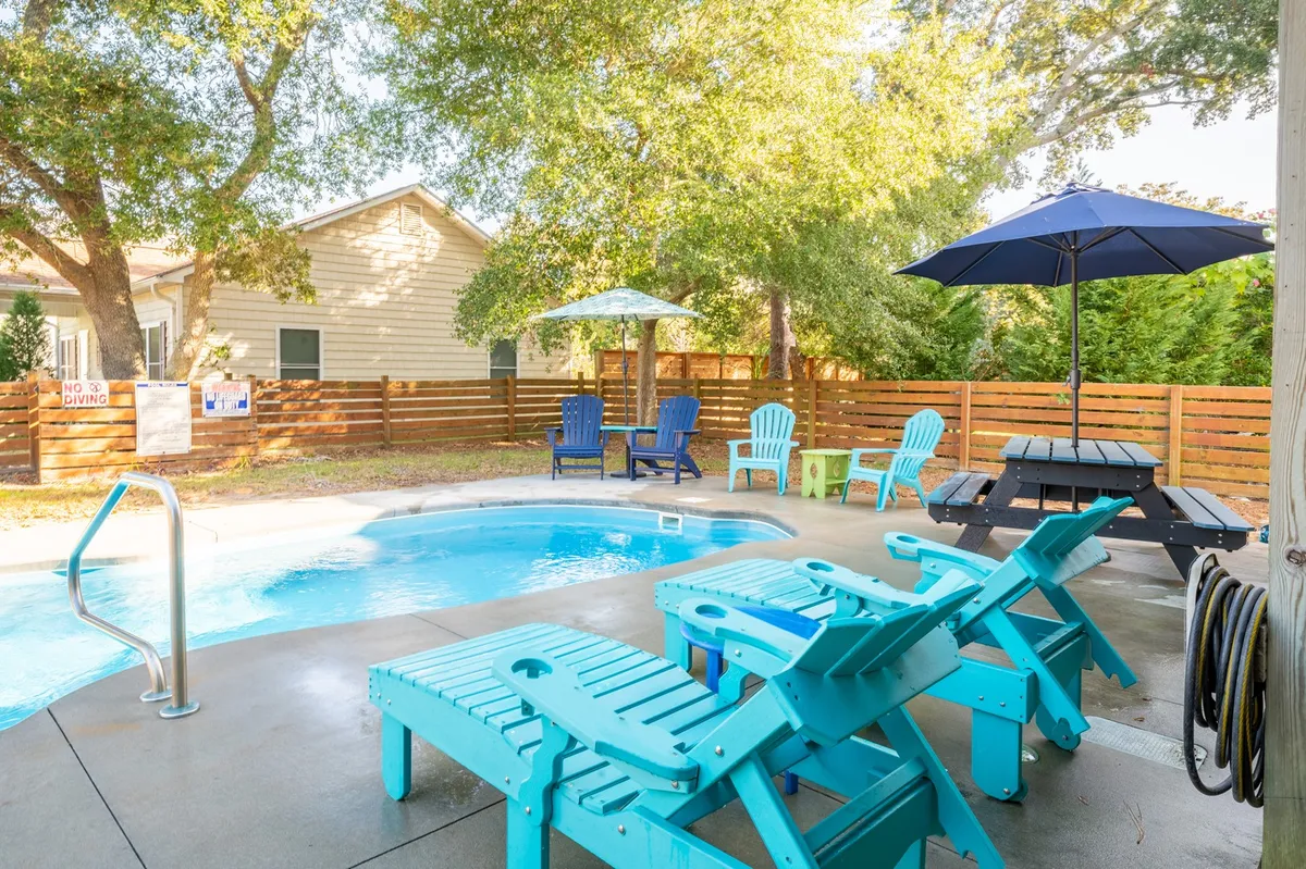 The hero image showcases a sparkling private pool surrounded by comfortable lounge chairs, a shaded umbrella, and a large picnic table. The inviting outdoor space is set up for swimming, sunbathing, outdoor dining, and relaxing—perfect for gatherings and family fun.